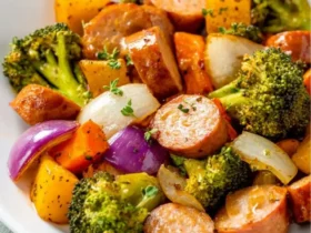 A white bowl filled with One-Pan Honey Garlic Kielbasa And Veggies featuring sliced sausage, broccoli, peppers, and onions.