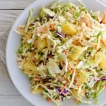 Fresh Pineapple Coleslaw with shredded cabbage, carrots, and pineapple chunks in a creamy dressing served in a white bowl.