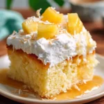 A slice of Pineapple Poke Cake with Coconut Cream topped with whipped cream, pineapple chunks, and toasted coconut flakes on a plate.