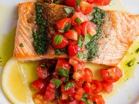 Pan-seared Salmon with Basil Sauce and Tomato Salad served on a white plate with fresh lemon.