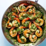 Shrimp With Chimichurri Sauce sizzling in a stainless steel skillet, topped with fresh green herb sauce.