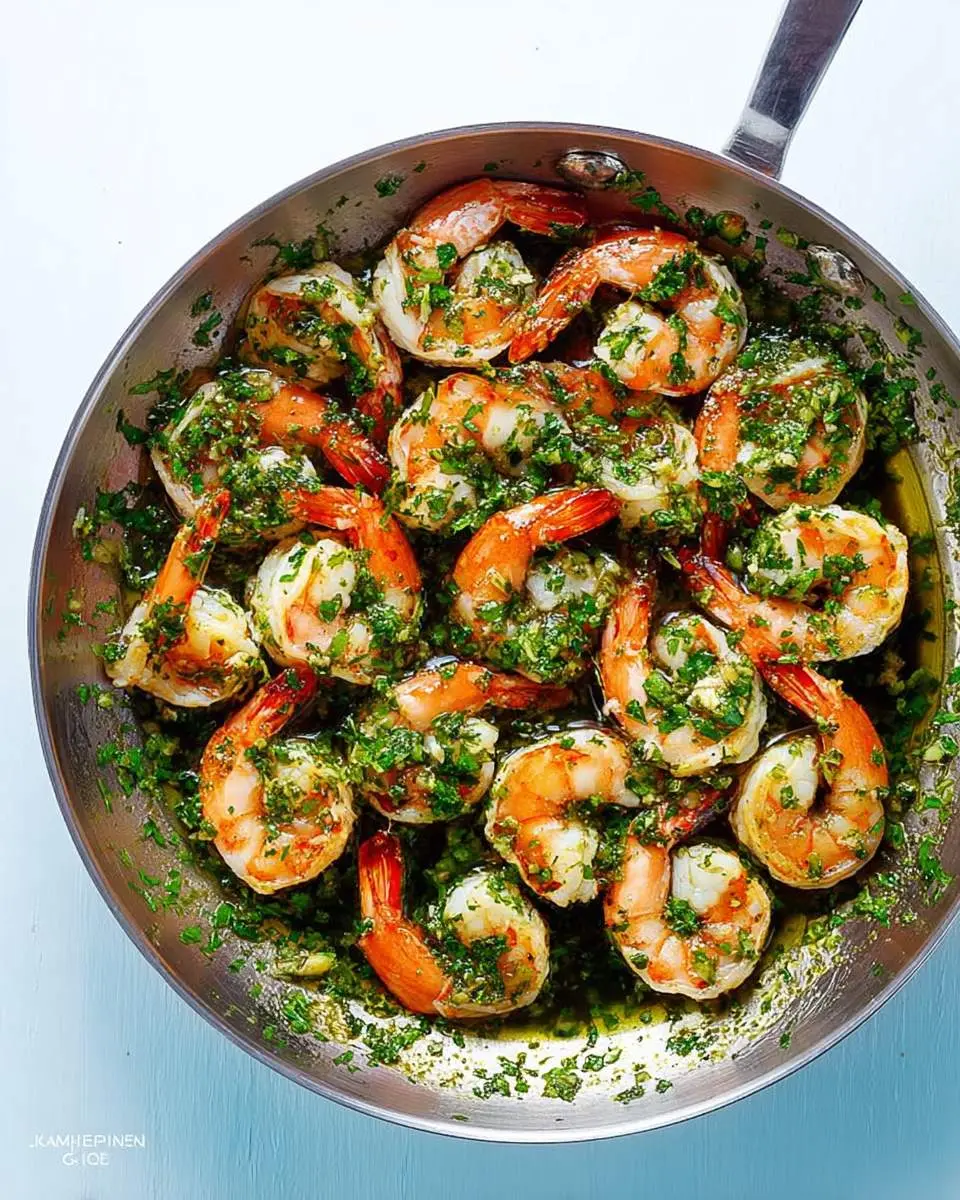 Shrimp With Chimichurri Sauce sizzling in a stainless steel skillet, topped with fresh green herb sauce.