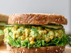 A close-up of a Smashed Chickpea Avocado Dill Pickle Sandwich on seeded bread with lettuce and cucumber slices.