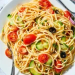 A bowl of fresh spaghetti salad with cherry tomatoes, cucumbers, black olives, and herbs in a white dish.
