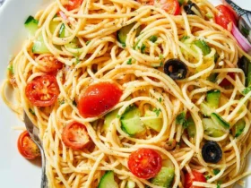 A bowl of fresh spaghetti salad with cherry tomatoes, cucumbers, black olives, and herbs in a white dish.