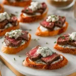 Elegant Steak Crostini with Boursin Cheese on toasted baguette slices, topped with fresh herbs.