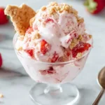 Creamy Strawberry Cheesecake Ice Cream topped with graham cracker crumbles and fresh strawberry chunks in a glass dish.