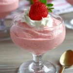 A glass dessert cup filled with creamy strawberry mousse topped with whipped cream and a fresh strawberry.