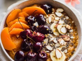 Sweet Potato Breakfast Bowl topped with fresh cherries, apricot slices, banana, almonds, and chia seeds in a ceramic bowl.