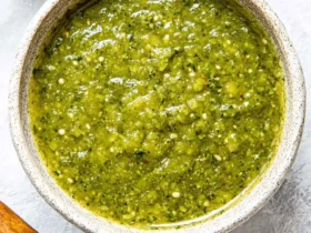 A rustic bowl filled with vibrant green Tomatillo Salsa Verde, with a wooden spoon and fresh jalapeño nearby.