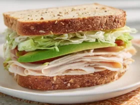A Turkey Avocado Sandwich with multigrain bread, sliced turkey, fresh avocado, lettuce, and tomato on a white plate.
