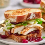 A toasted Turkey Brie Cranberry sandwich recipes featuring sliced turkey, melted brie, fresh greens, and cranberry sauce on golden bread.