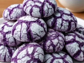 ube crinkle cookies 35 A stack of purple ube crinkle cookies with powdered sugar coating on a white plate beside a cup of tea.