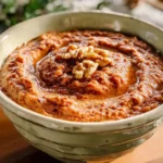 A rustic bowl of Walnut Romesco Sauce topped with chopped walnuts and drizzled with olive oil.