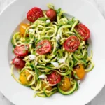 Fresh Zoodles with Summer Vegetables served in a white bowl, featuring spiralized zucchini, cherry tomatoes, and crumbled cheese.