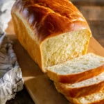 Freshly baked loaf of Amish White Bread with golden crust and soft interior, sliced on a wooden cutting board.