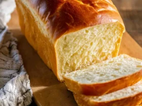 Freshly baked loaf of Amish White Bread with golden crust and soft interior, sliced on a wooden cutting board.