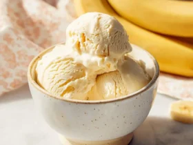 A ceramic bowl filled with creamy banana ice cream, surrounded by fresh banana slices and whole bananas in the background.