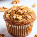 A freshly baked banana walnut muffin topped with crunchy walnuts sits on a white marble surface.