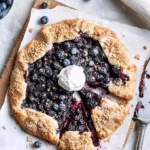 Rustic Blueberry Galette with Pie Crust topped with whipped cream and sliced on parchment paper.