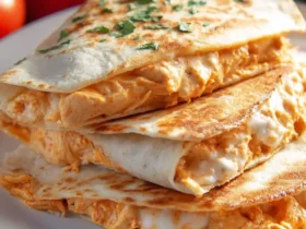 Stack of golden-brown Buffalo Chicken Quesadillas filled with creamy chicken and melted cheese, garnished with fresh herbs.