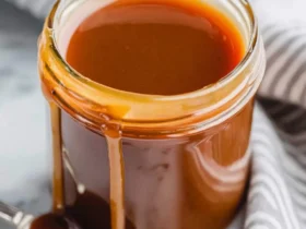 caramel sauce 47 A glass jar filled with rich, glossy caramel sauce with drips running down the side onto a marble surface.