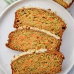 Three slices of moist Carrot Zucchini Bread with cream cheese frosting arranged on a white plate.