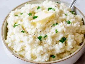 cauliflower mashed potatoes 37 A bowl of creamy cauliflower mashed potatoes topped with butter, chives, and black pepper.