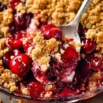 A spoonful of warm Cherry Crisp with golden crumble topping and juicy red cherries in a glass baking dish.