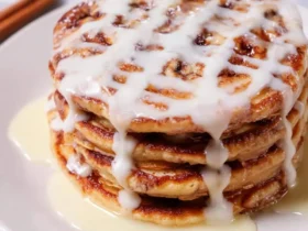 Stack of Cinnamon Roll Pancakes drizzled with cream cheese glaze on a white plate.