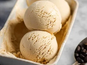 Three scoops of creamy coffee ice cream in a rectangular ceramic dish with coffee beans scattered nearby.
