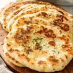 Golden brown Cottage Cheese Flatbread stacked on a wooden board, garnished with fresh herbs.