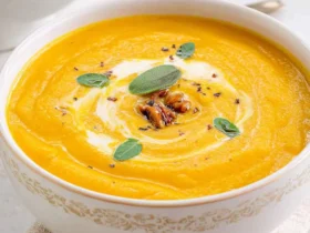 Creamy Crockpot Butternut Squash Soup in a white bowl topped with sage leaves, pecans, and a swirl of cream.