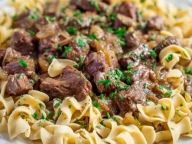 A plate of Crockpot French Onion Beef And Noodles topped with fresh parsley, featuring tender beef chunks and egg noodles.