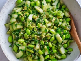 Cucumber Edamame Salad with sesame seeds and fresh herbs served in a white speckled bowl with a wooden spoon.