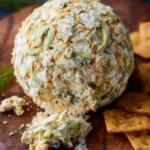 A Dill Pickle Cheese Ball covered in crushed crackers and fresh dill sits on a wooden board with crackers.
