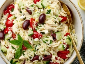 A bowl of Greek Lemon Chicken Orzo Salad with tomatoes, cucumbers, olives, feta, and fresh herbs.