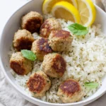 Greek turkey meatballs with lemon herb rice served in a white bowl with fresh lemon slices and mint leaves.