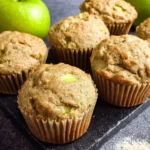 Freshly baked green apple muffins with visible apple chunks sit on a dark slate board with green apples in the background.