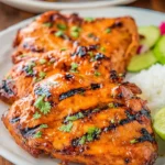 Grilled Honey Chipotle Chicken with char marks garnished with cilantro, served with rice and lime on a white plate.