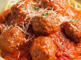 A bowl of Italian Meatballs on Parmesan Noodles topped with marinara sauce, grated cheese, and fresh herbs.