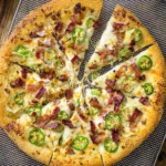 A sliced Jalapeno Popper Pizza topped with melted cheese, crispy bacon, and fresh jalapeño slices on a golden crust.