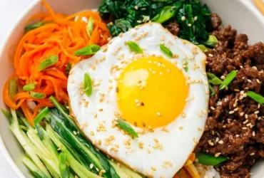 Korean Bibimbap Beef Bowl with rice, seasoned beef, vegetables, and a fried egg topped with sesame seeds.