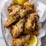 Crispy Lemon Parmesan Chicken Wings garnished with herbs and cheese, served in a wire basket with fresh lemon wedges.