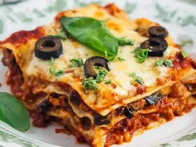 Low Carb Eggplant Lasagna 47 A slice of Low Carb Eggplant Lasagna topped with melted cheese, black olives, and fresh basil on a decorative plate.