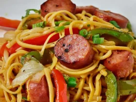Low Carb Lo Mein With Keilbasa & Peppers served on a white plate with colorful vegetables and sliced sausage.