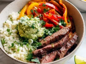 Low Carb Steak Fajita Bowls 50 Low Carb Steak Fajita Bowls with cauliflower rice, grilled peppers, guacamole, and lime wedges in a ceramic bowl.