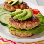 Low Carb Turkey and Zucchini Burgers stacked with lettuce and topped with fresh avocado slices on a white plate.