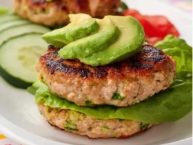 Low Carb Turkey and Zucchini Burgers stacked with lettuce and topped with fresh avocado slices on a white plate.