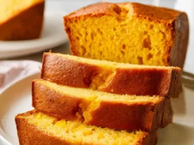Sliced mango bread loaf with golden crumb on a white plate, showing moist tender slices stacked in front.